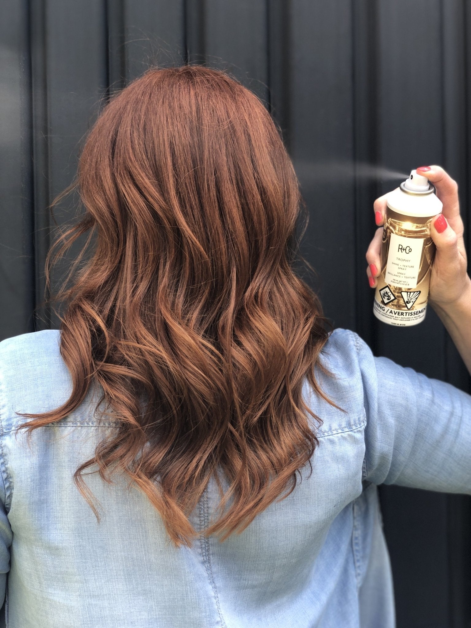 Model using TROPHY Styling Spray to add volume and shine to styled hair with a soft, natural finish